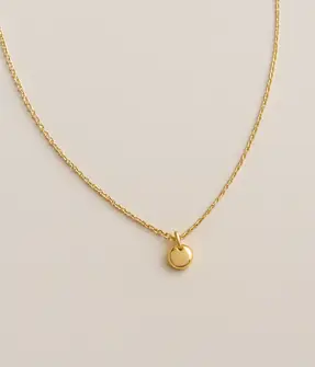Collar dorado con dije redondo Collar dorado minimalista con dije circular sobre fondo neutro, joya elegante y versátil para mujer.
